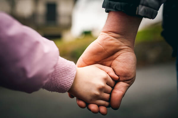Two ways to save money for a growing family. Detail of father and daughter holding hands.