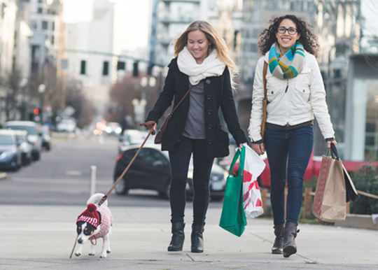 dos mujeres paseando por Portland con perro y bolsas de la compra navideña