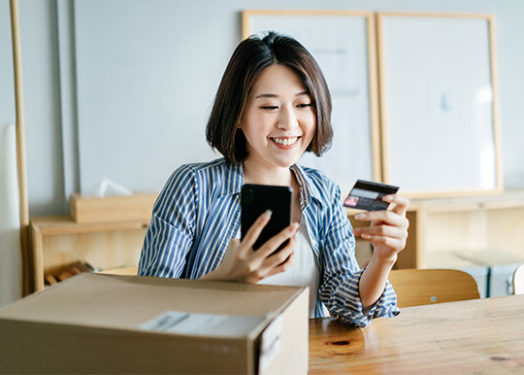 Cheerful businesswoman shopping online with smartphone and making mobile payment with credit card